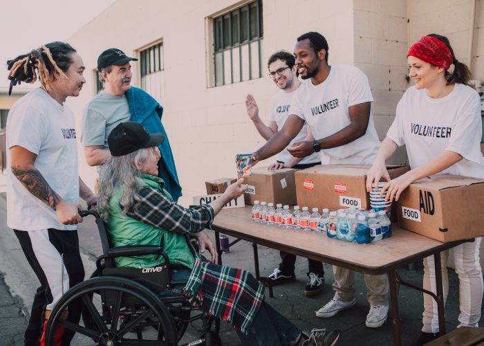 A Group of Volunteers Assisting an Elderly Person on a Black Wheelchair For Charity
